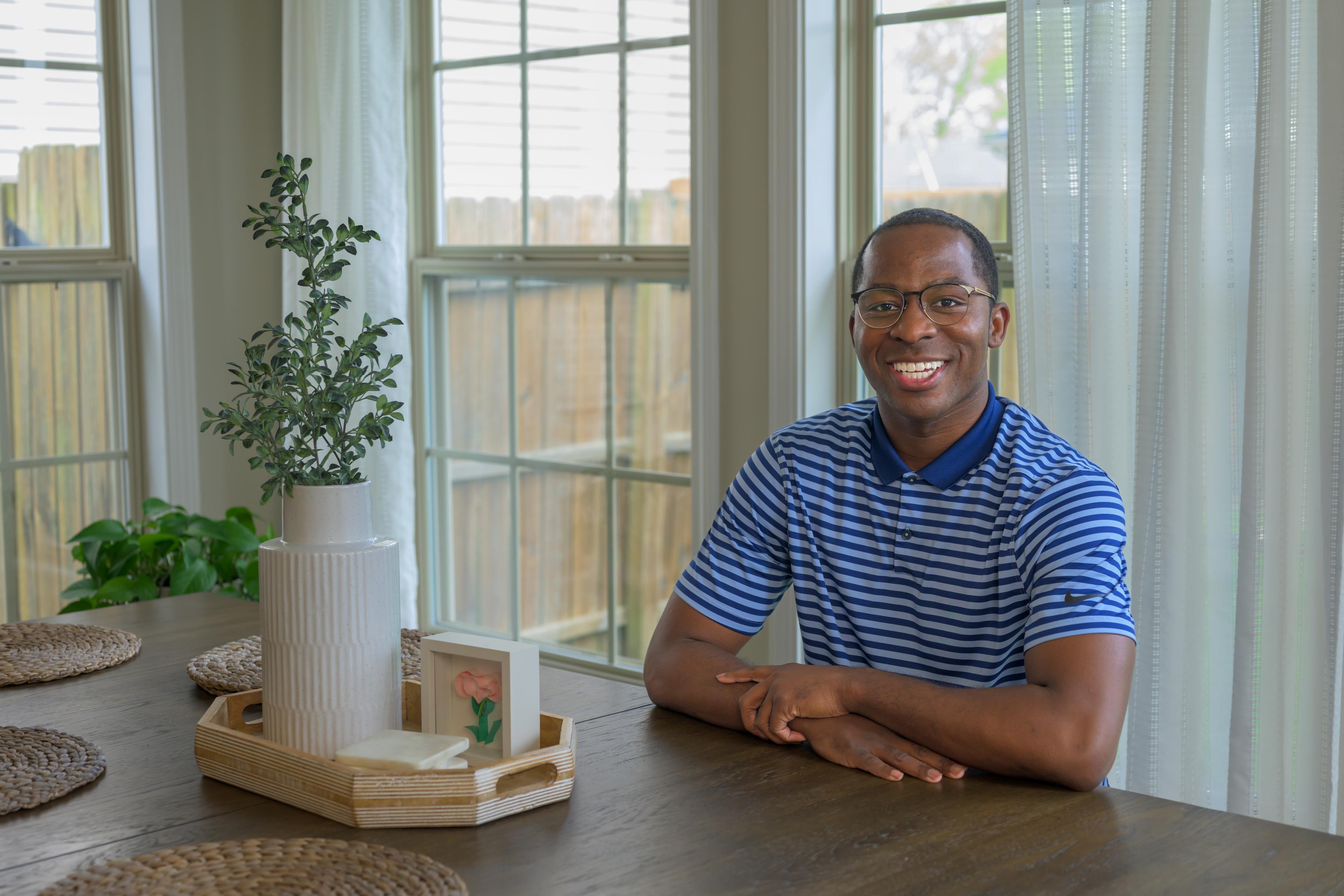 Dr. Anthony Myrks-Brewer '17 smiles for the camera while sitting at his dining room table.