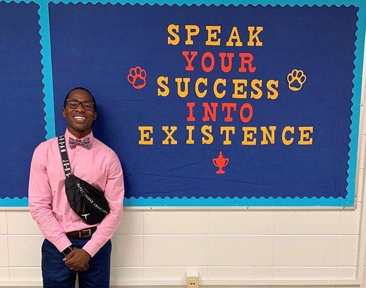 Dr. Anthony Myrks-Brewer '17 posing at his first job as a teacher after graduating from Berea College. The poster behind him reads "Speak your success into existence"